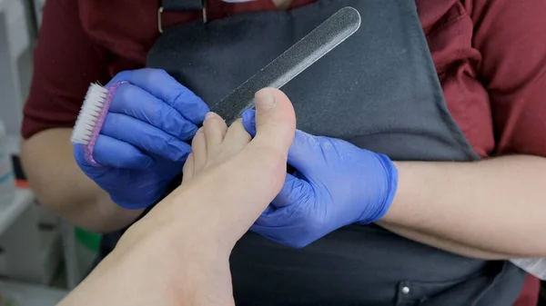 Maestro hace una pedicura a un cliente en un salón de belleza, utilizando una lima de uñas de los pies, pelando la piel de los pies. Primer plano, enfoque selectivo. —  Fotos de Stock