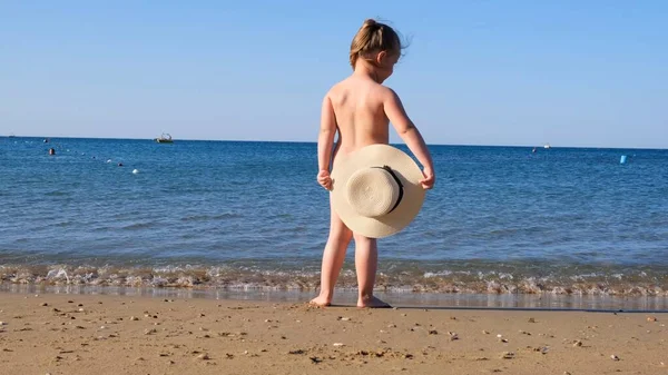 Забавная маленькая девочка 3 года в соломенной шляпе смотрит на море, вид сзади, крупный план. Детство, отношения, концепция летних каникул. Избирательный акцент на шляпе — стоковое фото