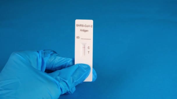 Hand in einem medizinischen Schutzhandschuh hält einen negativen SARS-CoV-2 Antigen-Schnelltest auf blauem Hintergrund — Stockvideo