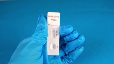 Koruyucu bir tıbbi eldiven içinde mavi bir arka planda negatif SARS-CoV-2 Hızlı Antijen Testi bulunur.