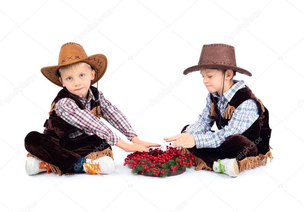 Two brothers in cowboy costumes are sitting by a christmas bonfire isolated on white background
