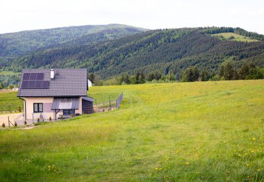Small house, solar panels as renewable source of energy. Mountain Village in summer afternoon. Solar panels on roof of house in high mountains. Copy space. CONCEPTS OF ECOLOGY