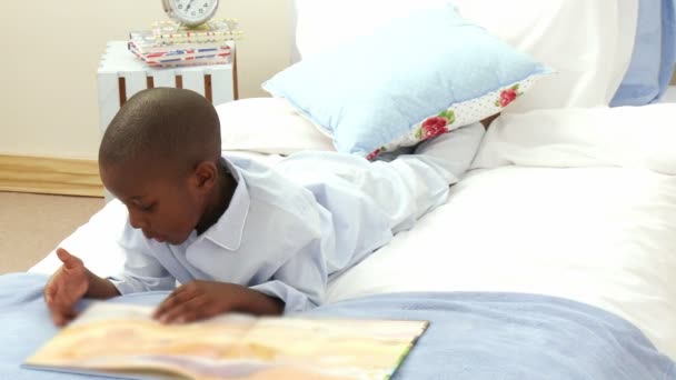Niño sonriente afroamericano leyendo en la cama — Vídeos de Stock
