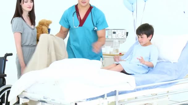 Доктор помогает маленькому мальчику лечь в постель — стоковое видео