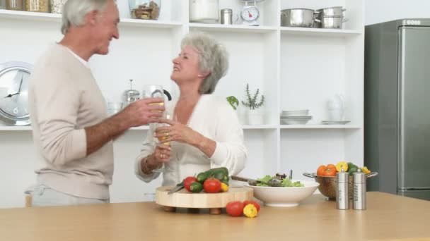 Кадри у високому визначенні усміхненої старшої пари готують салат на кухні та п'ють вино — стокове відео