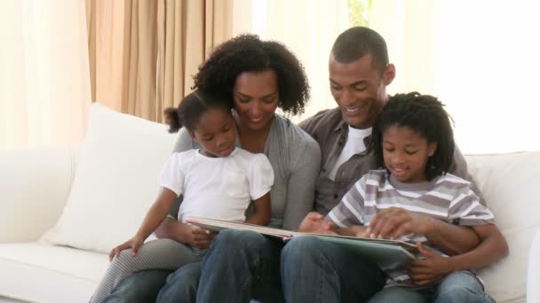 Pais afro-americanos e crianças lendo um livro na sala de estar — Vídeo de Stock