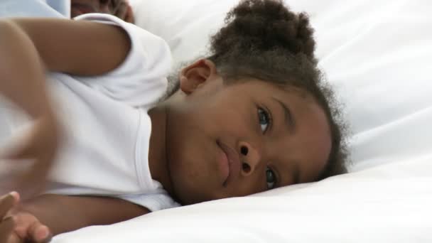 アフリカ系アメリカ人の小さな女の子が彼女の親のベッドで横になっています。 — ストック動画