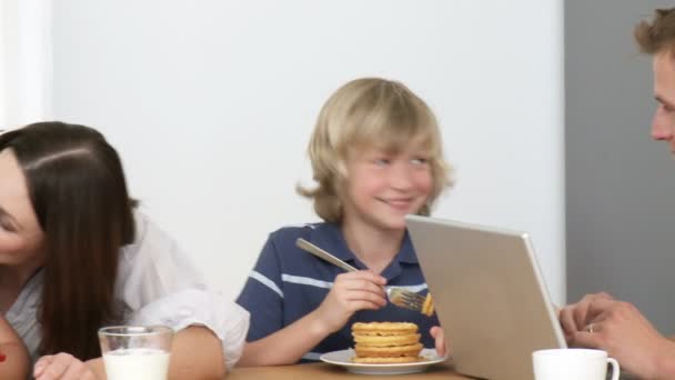 Panorama of father using a laptop and family eating sweets in the kitchen — Stock Video