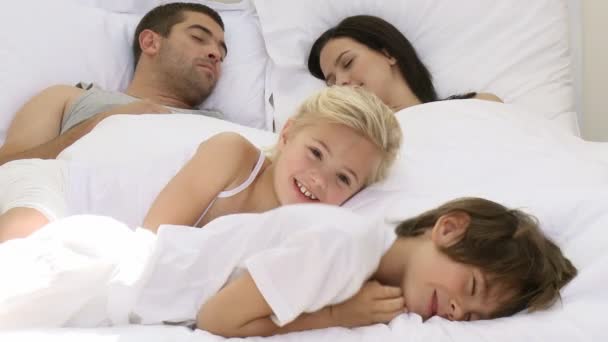 Fille souriante relaxant avec son frère et ses parents au lit — Video