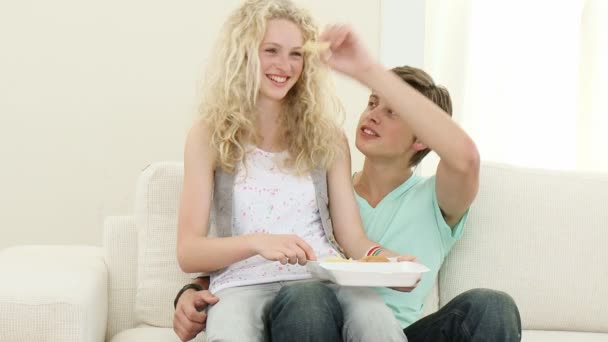 Casal de adolescentes comendo biscoitos no sofá — Vídeo de Stock