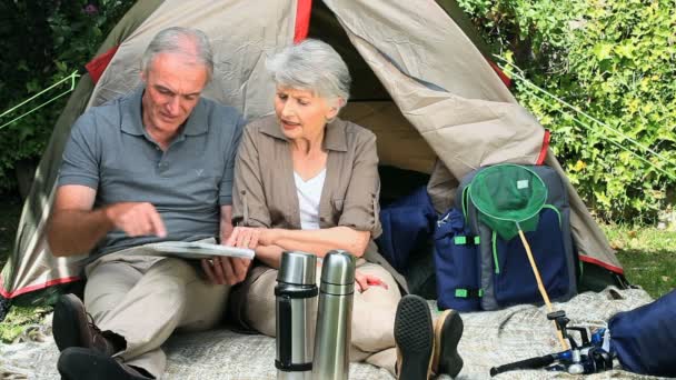Senioren kijken naar een kaart vergadering front van een tent — Stockvideo