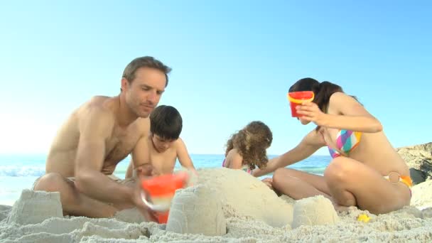 Glückliche Eltern bauen mit ihren Kindern eine Sandburg — Stockvideo