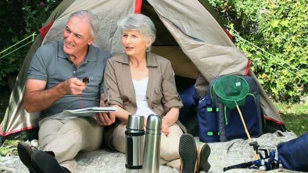 Seniors looking at a map sitting near a tent — Stock Video