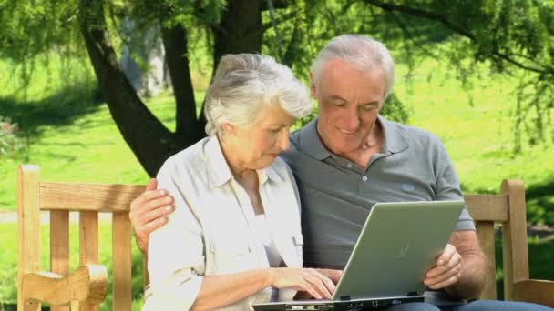 Couple mignon âgé regardant un ordinateur assis sur un banc — Video