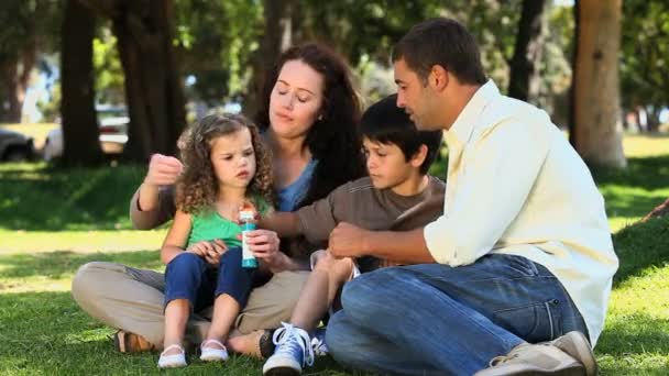 Rodzina spożywająca pęcherzyki, siedząc na trawie — Wideo stockowe