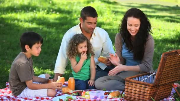 Gelukkige familie feesten op een picknick zittend op een tafellaken — Stockvideo