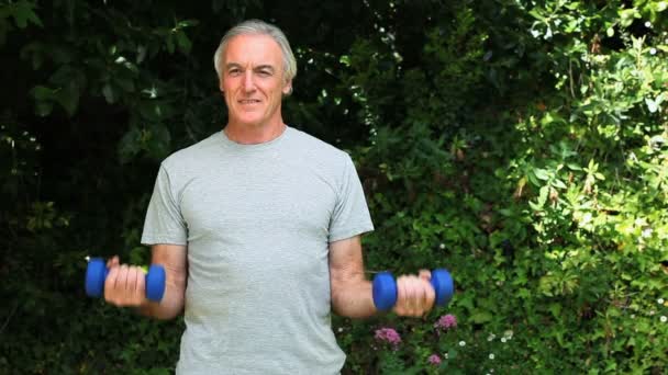 Літній чоловік працює м'язами з гантелями — стокове відео