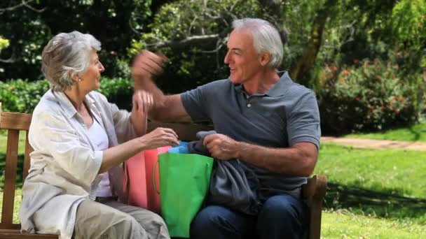 Old man looking at clothes with his wife after shopping on a bench — Stock Video