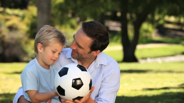 Papá y su hijo jugando con una pelota de fútbol sentado en la hierba — Vídeo de stock
