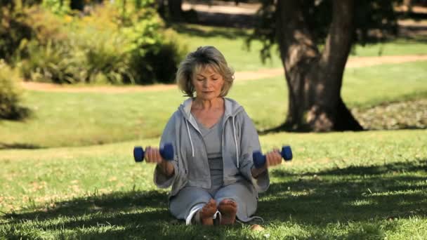 Femme âgée travaillant ses muscles avec des haltères sur l'herbe — Video