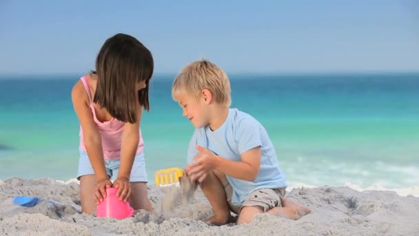 Lindo chico construyendo un castillo de arena con su hermana — Vídeos de Stock