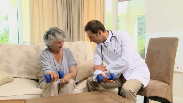 Joven médico mostrando a una anciana el uso de pesas — Vídeos de Stock