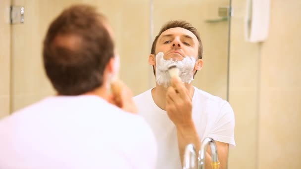 Handsome man shaving his beard in front of a mirror — Stockvideo