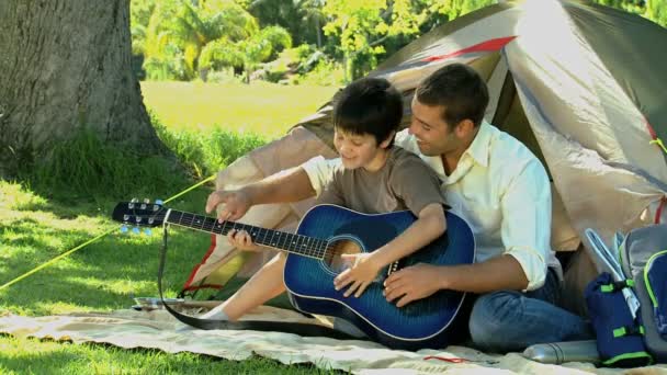 Father teaching guitar to his son in front of a tent — Stock Video