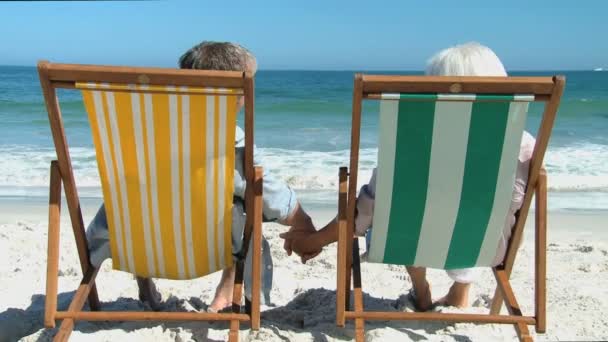 Pareja anciana mirando al océano sentada en sillas de playa — Vídeos de Stock