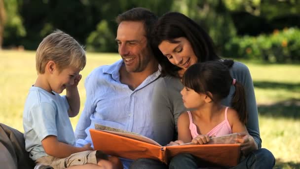 Família olhando para um livro sentado na grama — Vídeo de Stock