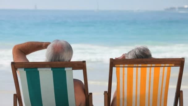 Bejaarde echtpaar kijken naar de oceaan zittend op het strandstoelen — Stockvideo