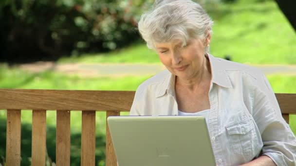 Seniorin blickt auf Laptop, der auf Bank sitzt — Stockvideo