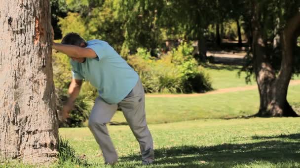 Vieil homme faisant des exercices d'étirement contre un arbre — Video