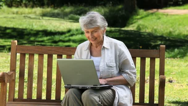 Alte Frau blickt auf einen Laptop, der auf einer Bank sitzt — Stockvideo