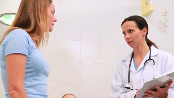 Доктор разговаривает с матерью, пока ее дочь лежит на больничной койке — стоковое видео
