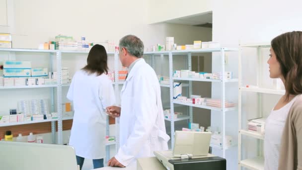 Male pharmacist talking to a colleague in front of a female client — Stock Video