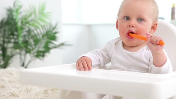 Baby sitzt und beißt Orangenlöffel — Stockvideo