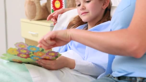 Smiling woman giving a teddy bear to a smiling girl in a bed — Stock Video