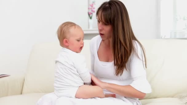 Woman sitting on the sofa and playing with baby in her legs — Stock Video