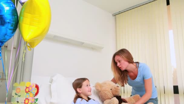 Lächelnde Frau schenkt einem lächelnden Mädchen in einem Bett einen Teddybär — Stockvideo