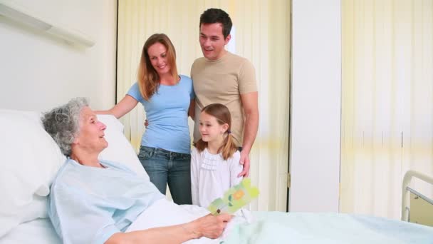 Family standing together around a hospital bed while a patient is reading a card — Stock Video