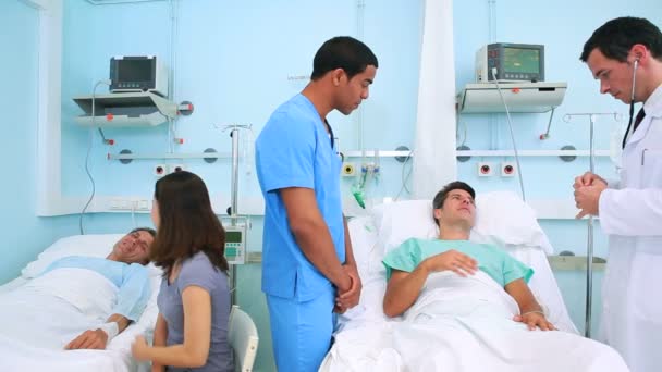 Medico utilizzando il suo stetoscopio su un paziente accanto a un infermiere maschio — Video Stock