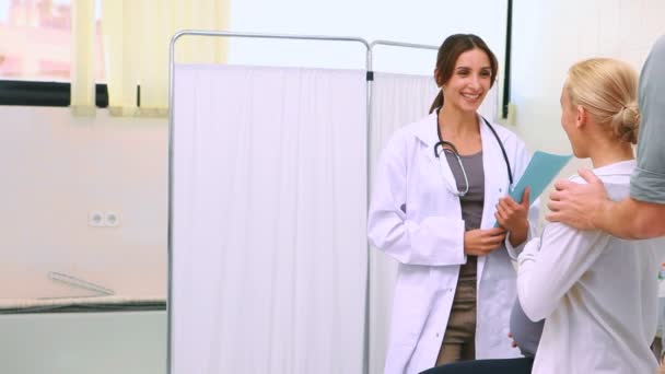 Kadın doktor hamile bir kadın ve kocası konuşurken dosyaları tutan — Stok video