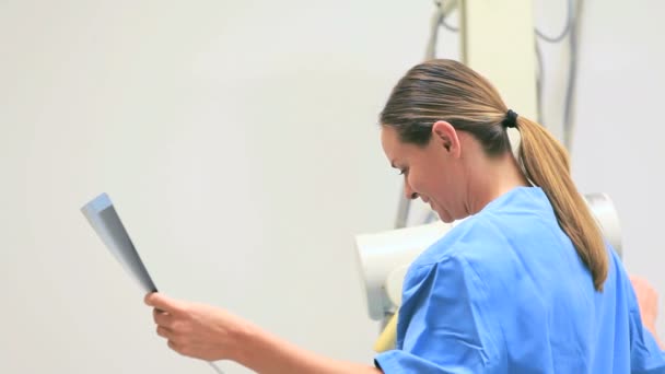 Smiling nurse holding x-ray while proceeding a radiography on a patient — Stock Video