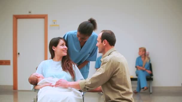 Enfermera sonriente detrás de una madre y un padre con su bebé en una silla de ruedas — Vídeo de stock