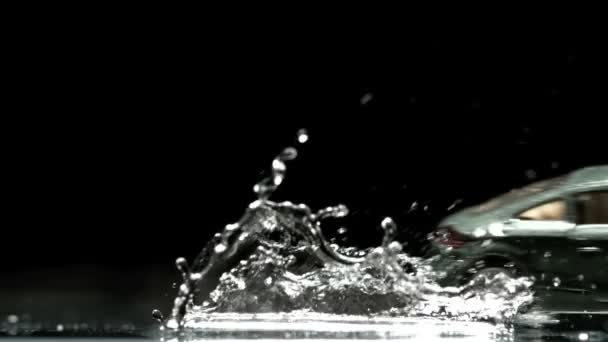 Игрушечный автомобиль, катящийся по воде и плещущийся на черном фоне — стоковое видео