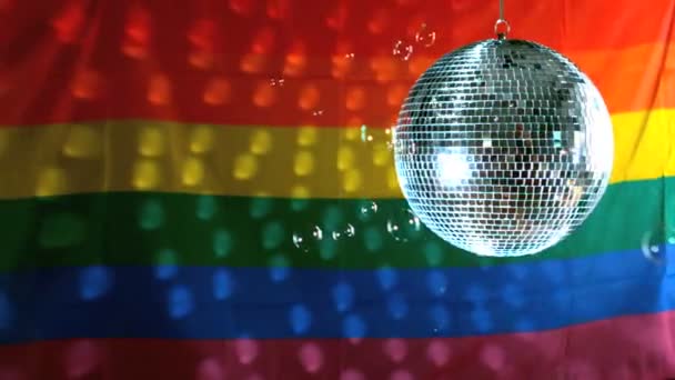 Glänzende Discokugel dreht sich mit schwimmenden Blasen gegen Regenbogenfahne — Stockvideo