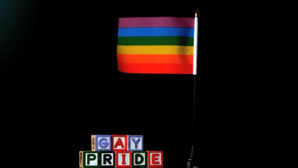 Regenboogvlag waait in de wind naast homo trots blokken op zwarte achtergrond — Stockvideo