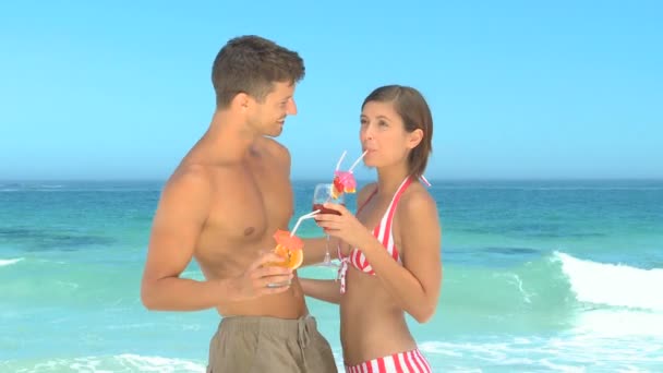 Сладкая пара делится коктейлями на пляже — стоковое видео