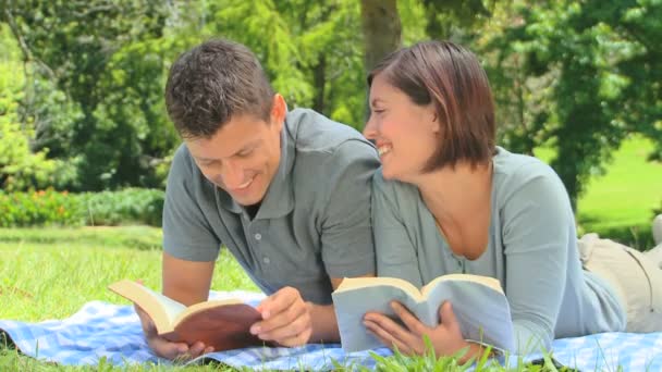 Jovem casal lendo um livro enquanto deitado na grama — Vídeo de Stock